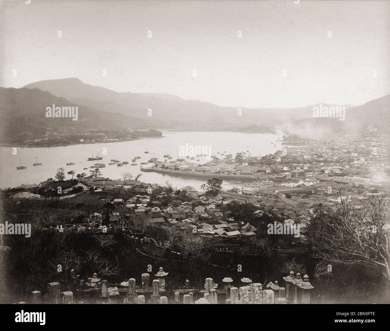 [ 1870s Japan - Nagasaki Harbor ] —   View on the Oura Foreign Settlement, Dejima and Nagasaki Harbor from a graveyard at the hillside above Juzenji temple (十善寺上の山) in Nagasaki, sometime between 1869 (Meiji 2) and 1876 (Meiji 9).  Beyond Dejima, the harbor stretches all the way to the Urakami area. This was later reclaimed, greatly reducing the size of the bay.  19th century vintage albumen photograph. Stock Photo