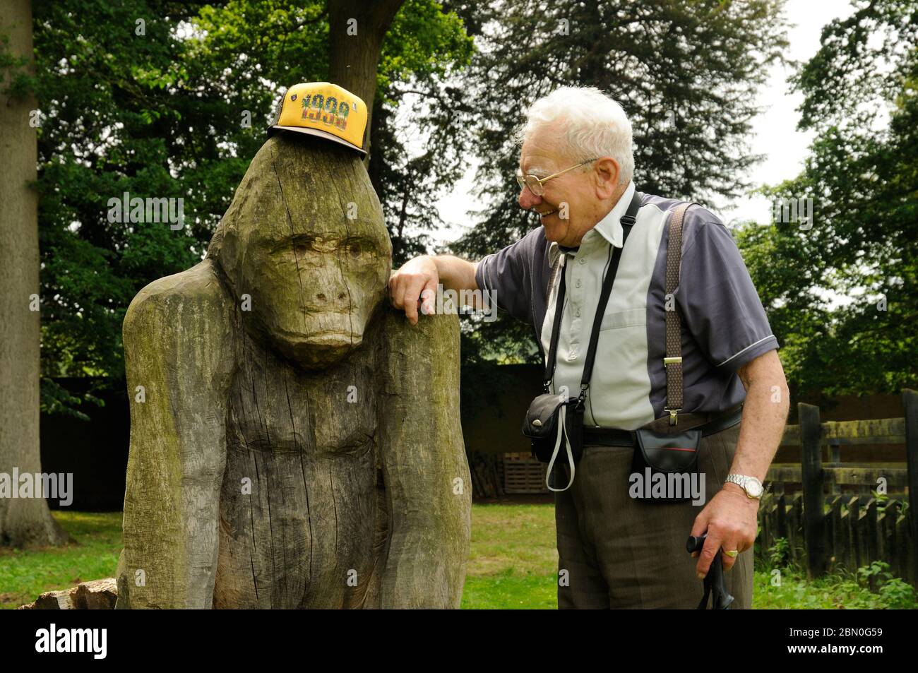 Elderly man having fun with his baseball cap and a carved wooden gorilla at the Elsham Hall country park, Lincolnshire, England Stock Photo
