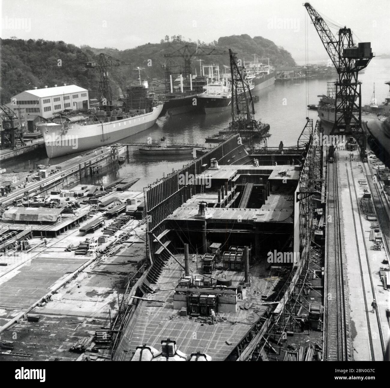 [ 1960s Japan - Japanese Shipyard ] —   Ship construction at the Uraga Dock Company (浦賀船渠株式会社) in Uraga (浦賀), a subdivision of Yokosuka in Kanagawa Prefecture, Japan, ca. 1960 (Showa 35).  The Uraga Dock Company was founded in 1869 (Meiji 2) by Admiral Enomoto Takeaki (榎本 武揚, 1836–1908), one of the founders of the Imperial Japanese Navy.  By 1919 (Taisho 8), it was considered one of the largest and best equipped private shipyards in the world.  20th century gelatin silver print. Stock Photo