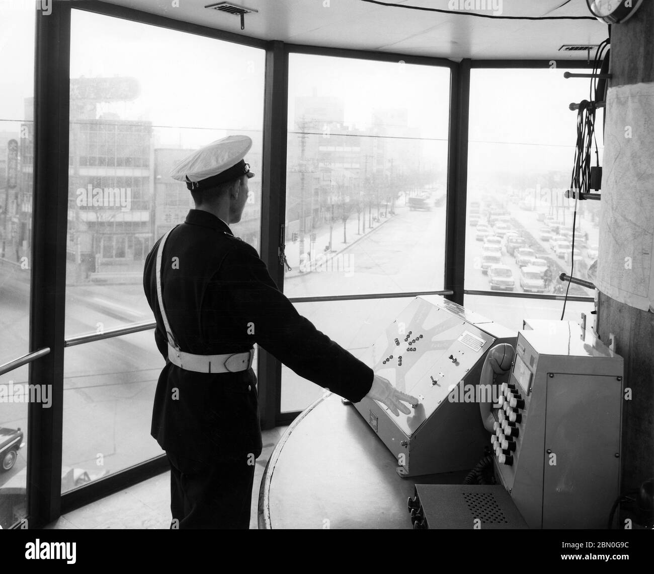 [ 1960s Japan - Ikebukuro Traffic Control Tower, Tokyo ] —   A Japanese police officer observes the traffic from the Traffic Control Tower (コントロールタワー・操車室) at the Mutsumata Rotary (六ツ又交差点) in Ikebukuro, Tokyo, ca. 1965 (Showa 40).  The 11 meter high tower started operations in November 1962 (Showa 37) and reduced the accidents that took place at this location from several hundreds to just a few dozen.  The tower was torn down on August 22, 1968 (Showa 43) to allow construction of the elevated highway Route 5.  20th century gelatin silver print. Stock Photo