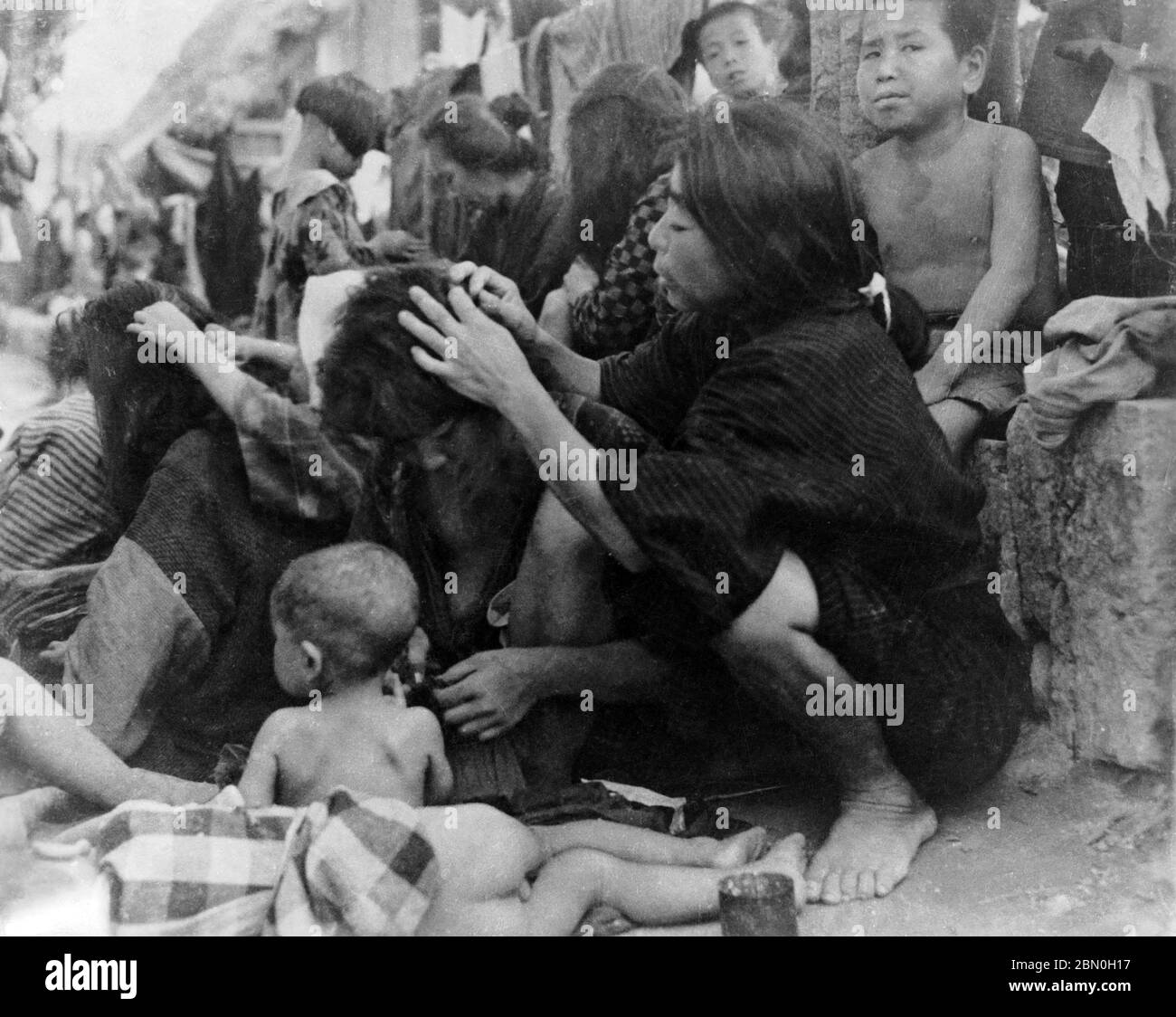[ 1945 Japan - WWII Internment Camp, Saipan ] —   Japanese women delousing each other at WWII Susupe Internment Camp (ススッペキャンプ) in Saipan, ca. 1945 (Showa 20).  The camp was opened in 1944 (Showa 19) to house 13.000 Japanese civilians and 5.000 Chamorros, Kakanas and Koreans. It was closed on July 4, 1946 (Showa 21).  The US capture of the Northern Marianas in July 1944 resulted in the first US occupation of Japanese territory.  20th century gelatin silver print. Stock Photo