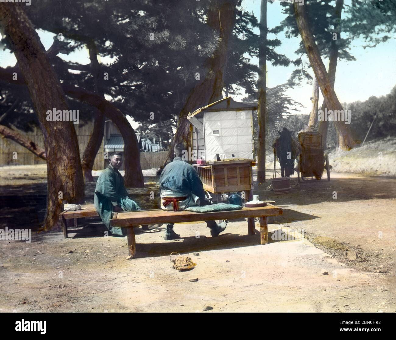 [ 1900s Japan - Japanese Road Side Tea Stand ] —   Two boys having tea at the wayside stand of a tea pedlar. A horse and cart can be seen in the back.  Japanese photographer Kozaburo Tamamura featured the same photograph in his book The Tea in Japan, published in 1908 (Meiji 41), conveniently dating this photograph to before this date.  19th century vintage glass slide. Stock Photo