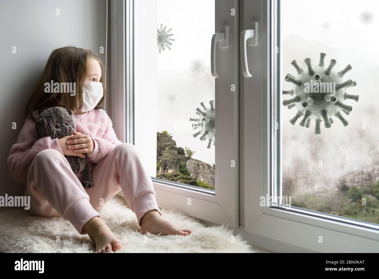 Coronavirus and quarantine concept, sad kid in medical mask looks out window, little girl sits on windowsill safe from corona virus during COVID-19 pa Stock Photo