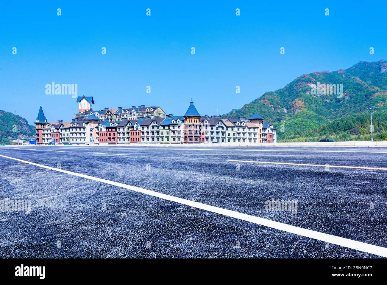 The empty car-free highway and the European-style building castle, in the distance are green mountains. Stock Photo