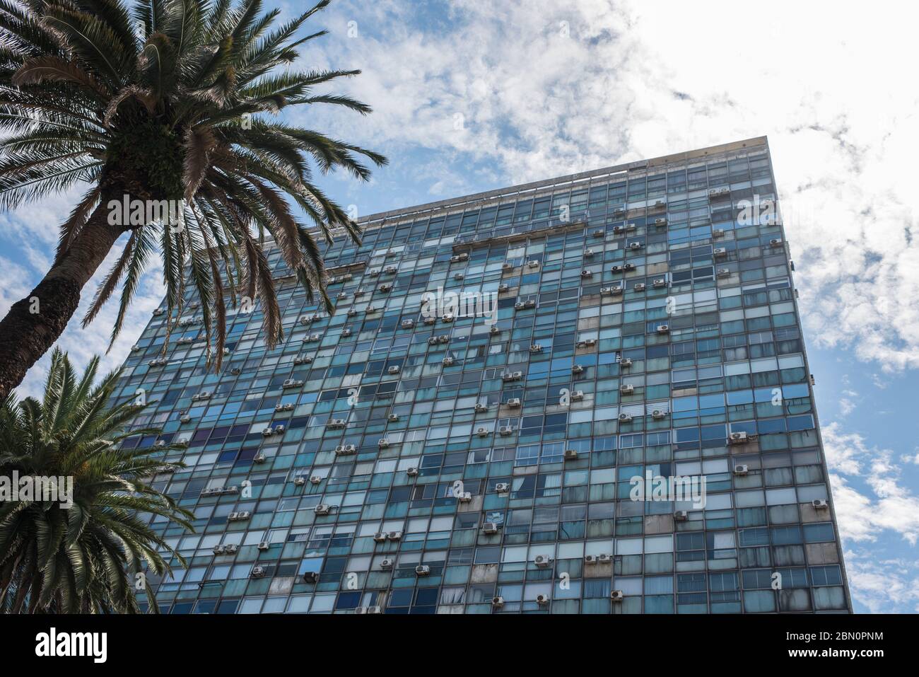 Montevideo / Uruguay, Dec 29, 2018: exterior view of a glazed building with many air conditioner machines hanged, palms and a sunny sky Stock Photo