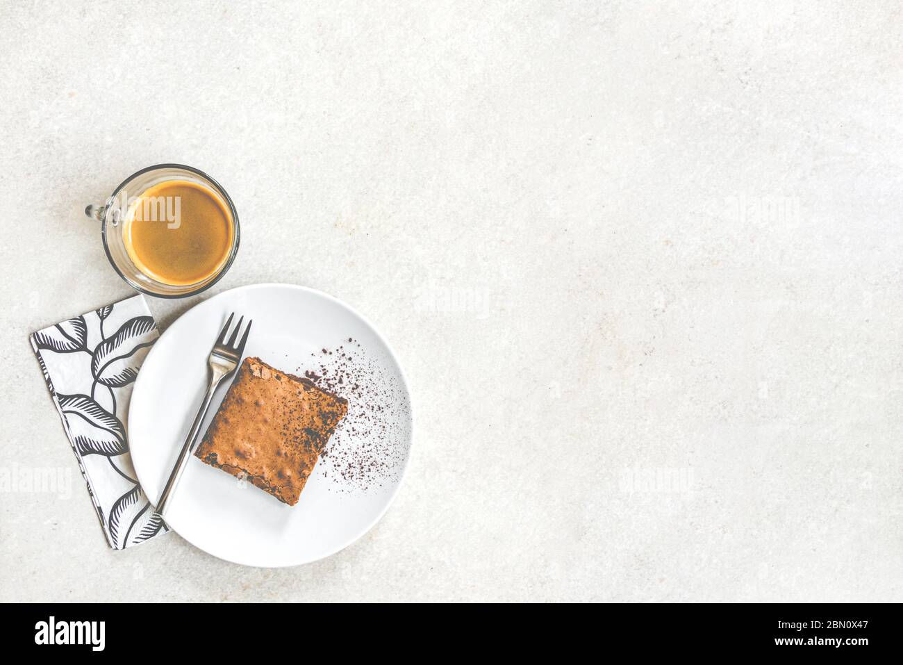 Top view of a cup of coffee and a dessert plate with brownie cake over white rustic background. Stock Photo