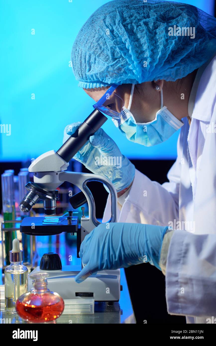 Laboratory worker in medical hat, mask and gloves looking through microscope Stock Photo Alamy