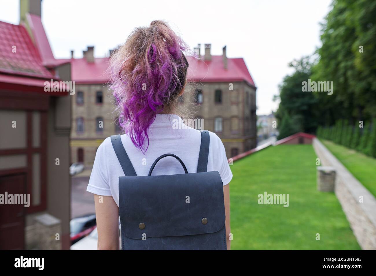 Portrait of teenage girl with backpack standing back looking at school building Stock Photo
