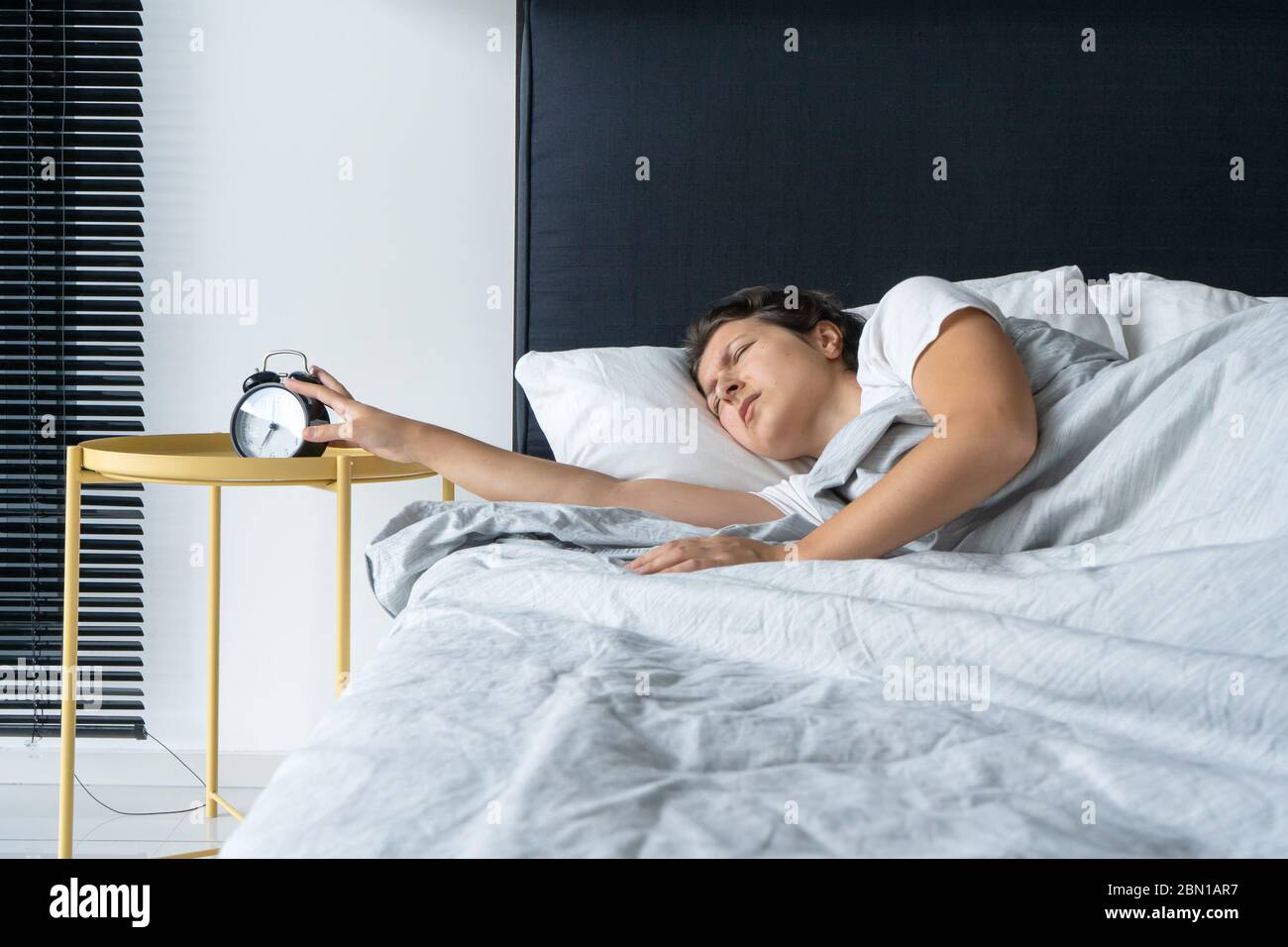 The girl turns off the annoying alarm clock to continue sleeping. Get