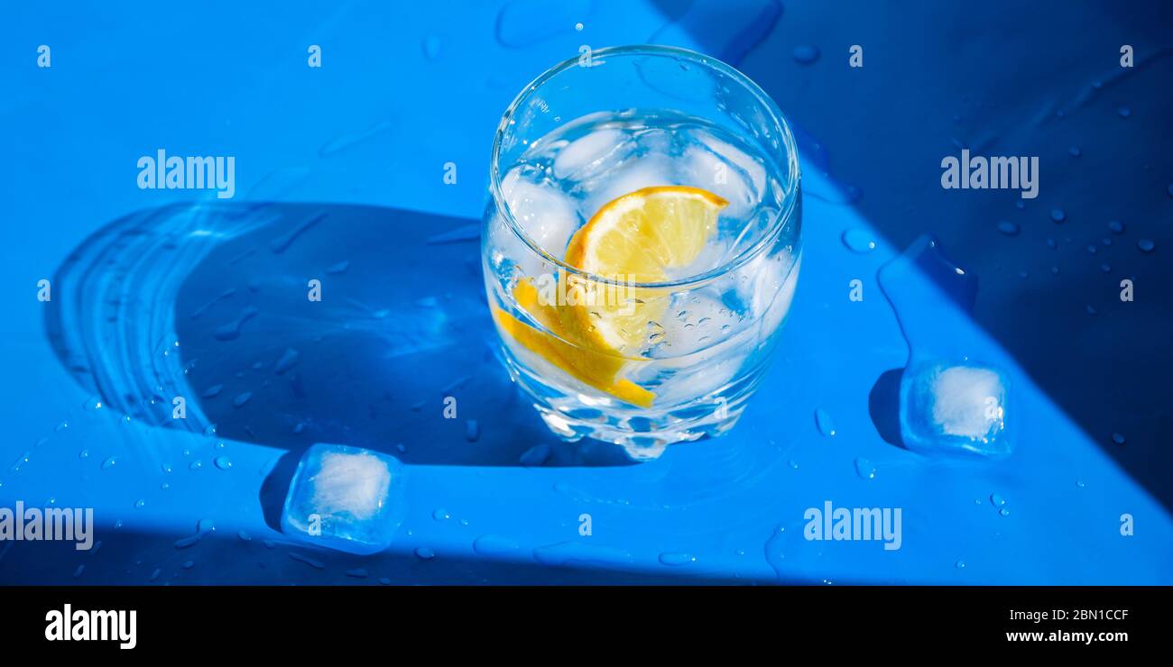 A glass of refreshing water with ice and lemon on a blue background. Heat concept, fresh. Natural light. Flat lay, top view, copy space Stock Photo