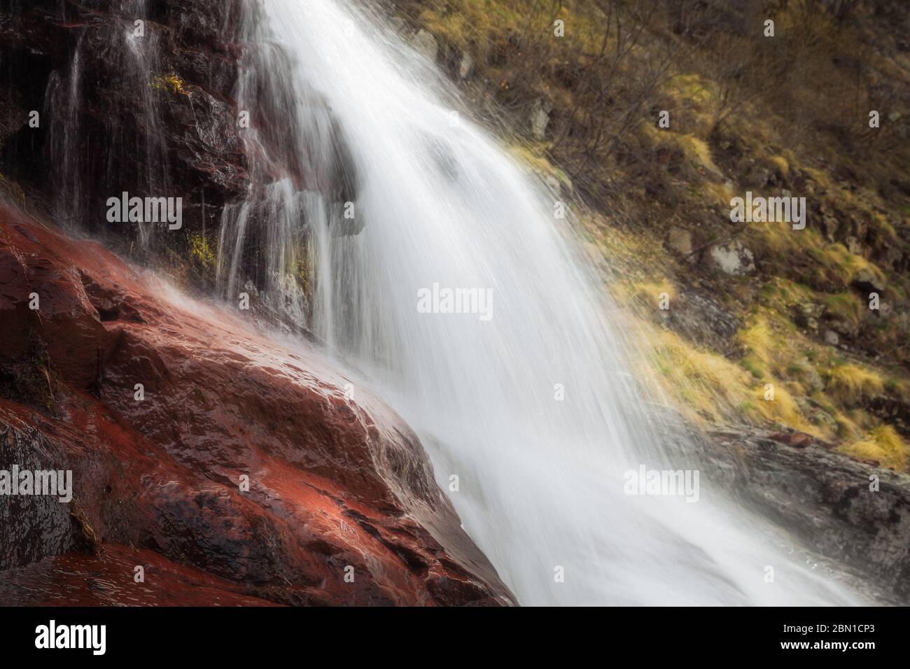 Stunning close up details of powerful waterfall cascading down the red, wet rocks and soft, background sunit golden grass Stock Photo