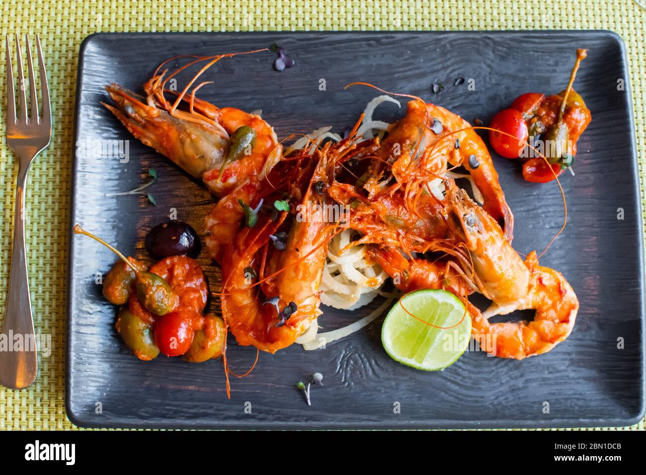 Sauteed shrimps in tomato, capers and olives sauce. Black plate in a