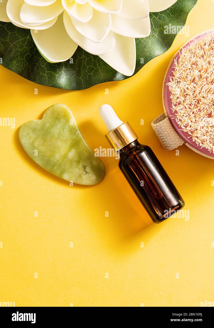 Dry body brush, oil bottle and gua sha massager at yellow background