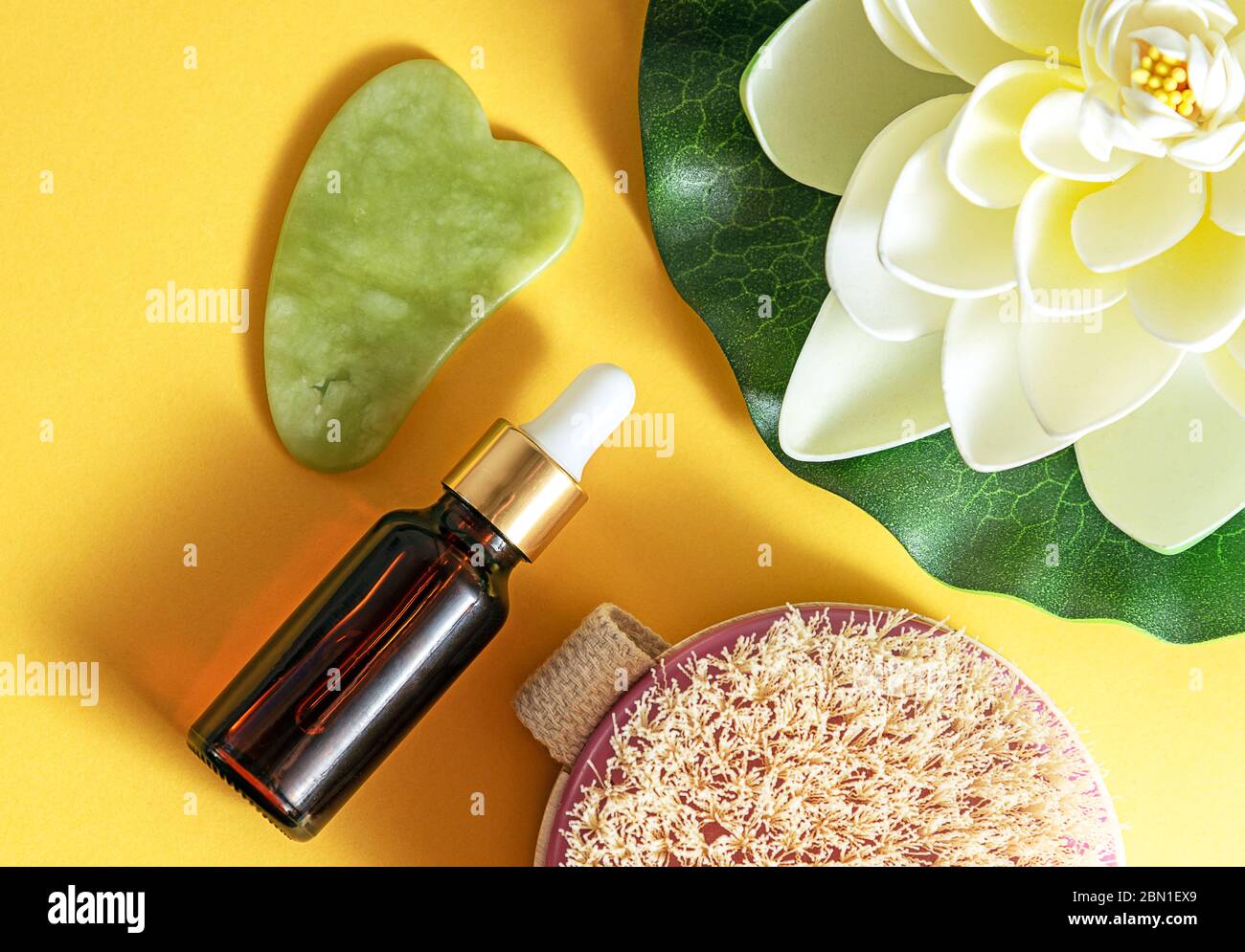 Dry body brush, oil bottle and gua sha massager at yellow background