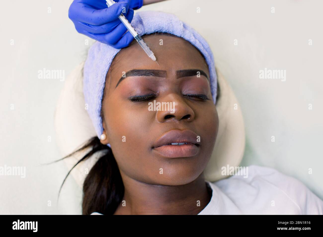 Hands of cosmetologist making injection in face. Young African woman