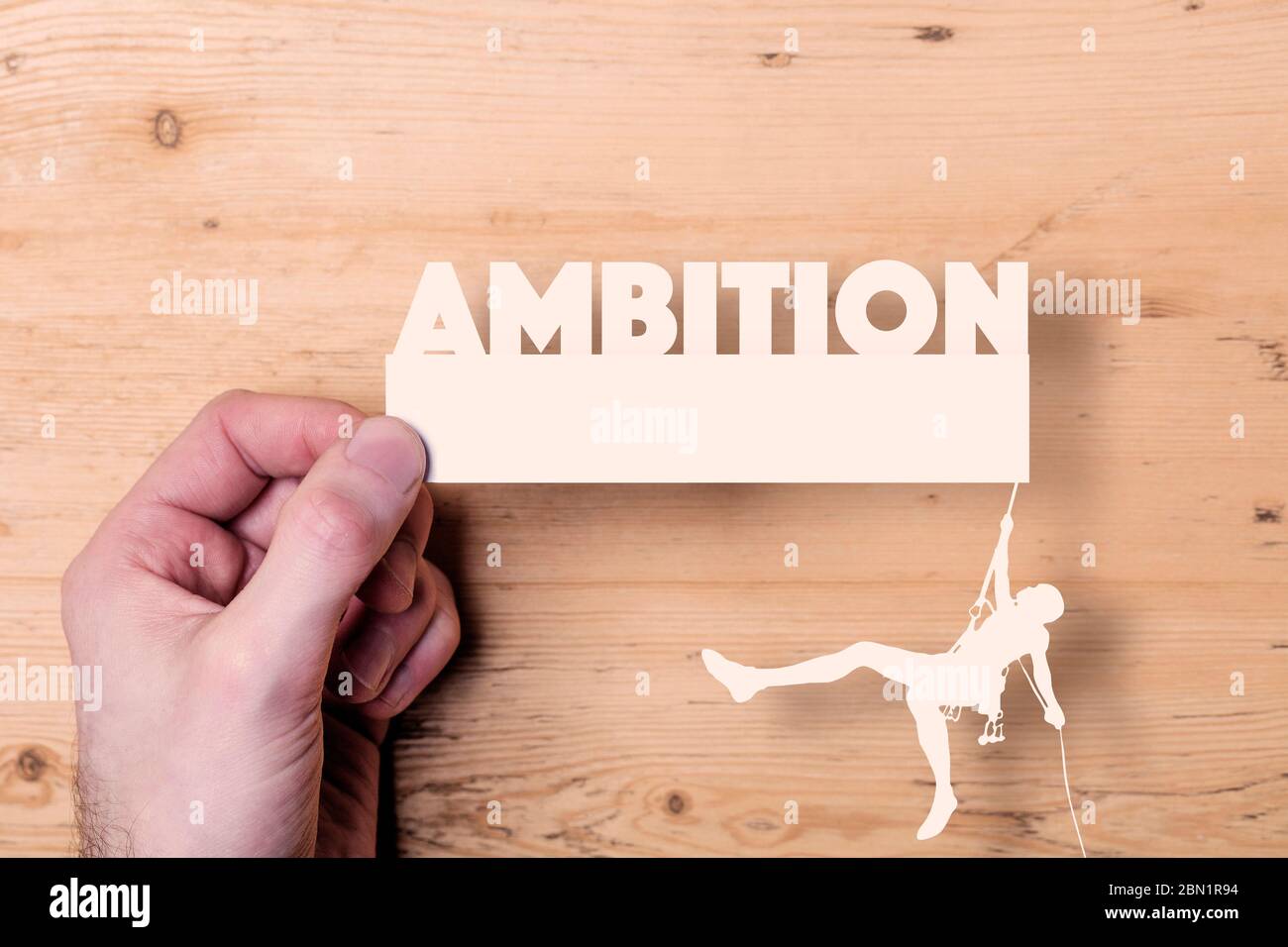 A paper cutout of a climber reaching the word Ambition. Business concept Stock Photo