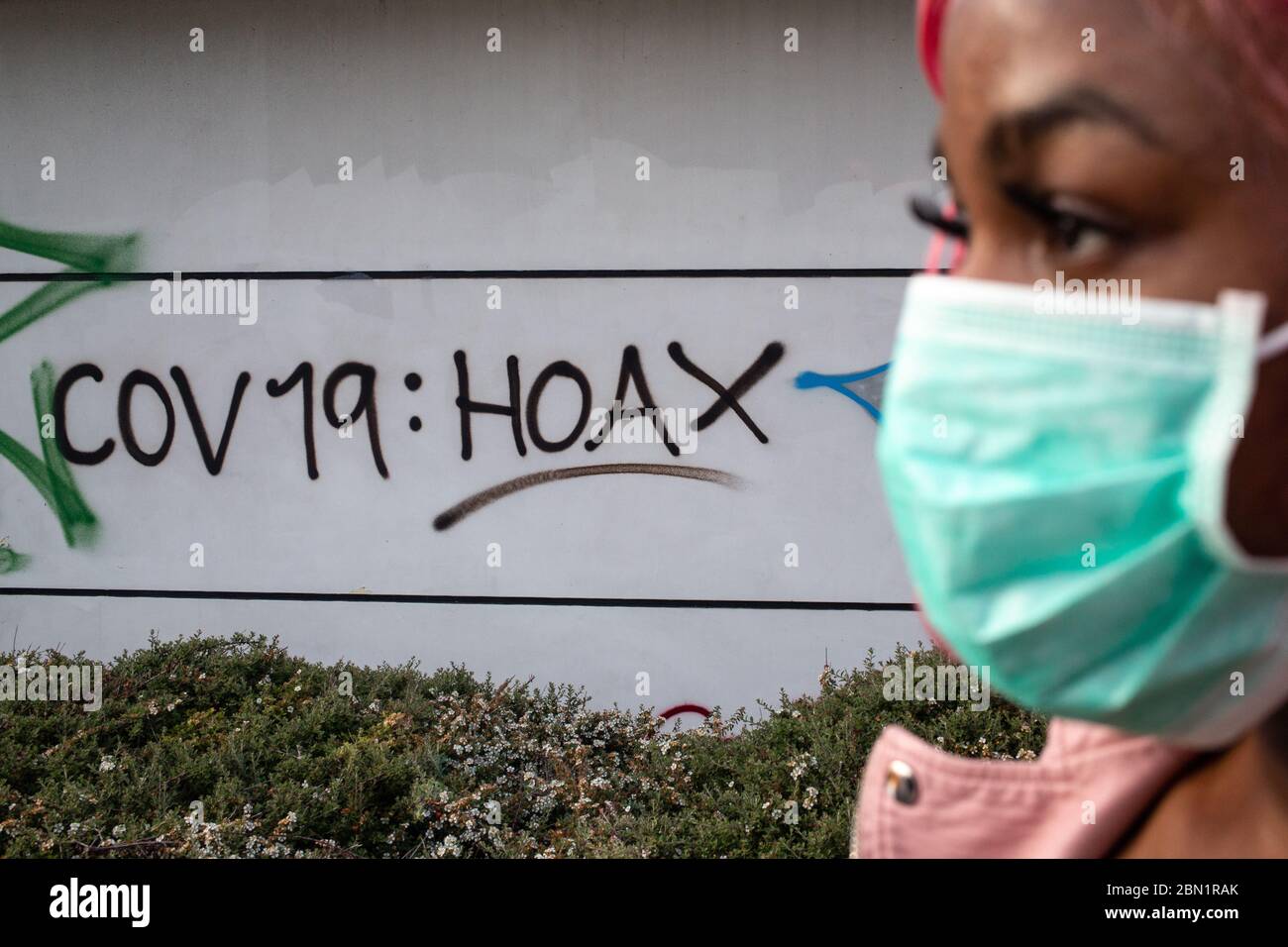 London UK 9th May 2020 A woman wearing a surgical mask walks past anti covid-19 graffiti in south London. Stock Photo