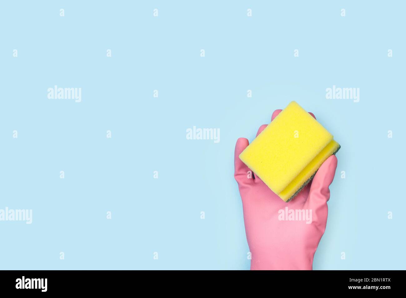 A hand with a pink rubber glove holding a cleaning sponge on a light ...