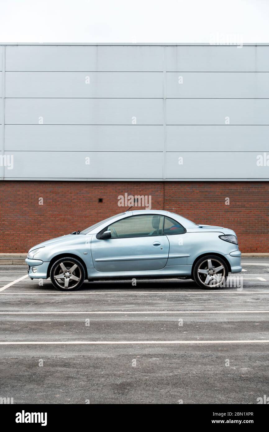 A Peugeot 206 CC compact coupe, parked in front of a grey prefabricated retail unit in Consett, County Durham, UK Stock Photo