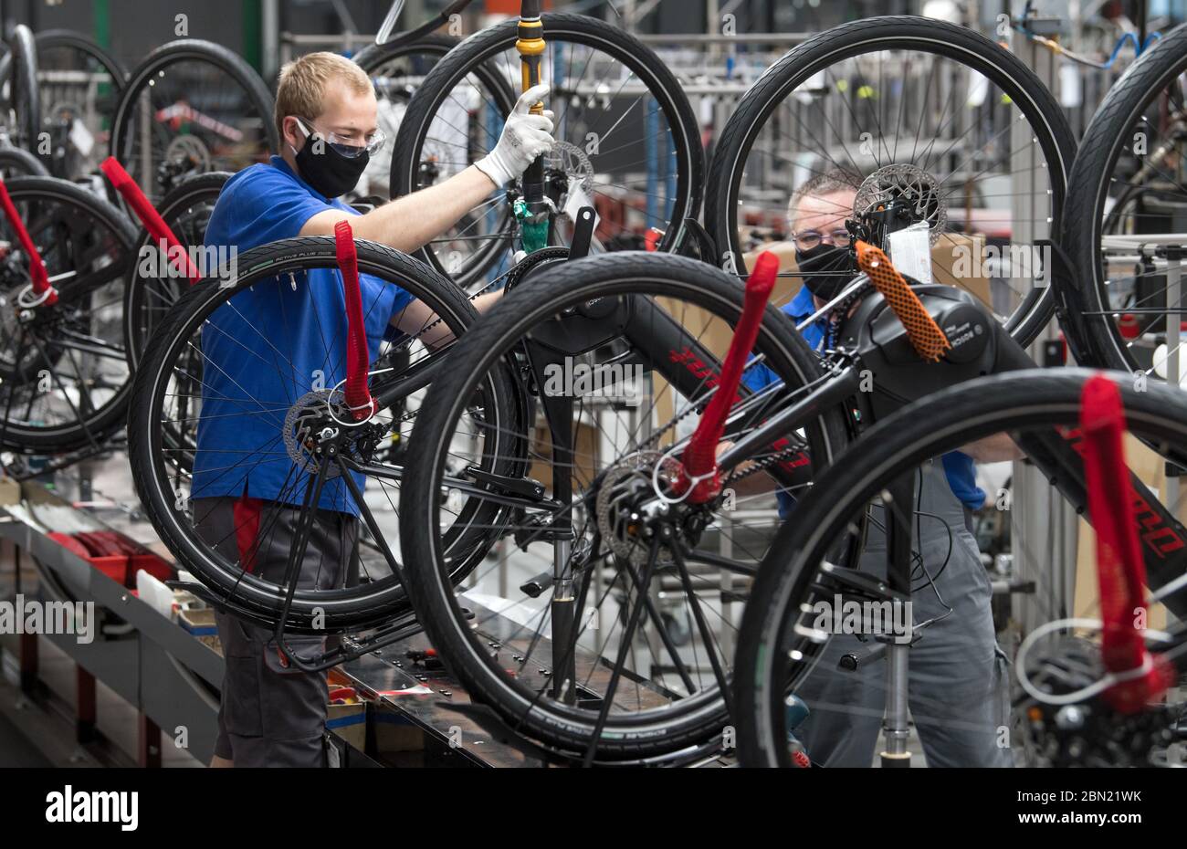 Hartmannsdorf, Germany. 12th May, 2020. Employees of the bicycle  manufacturer Diamant assemble electric trekking bikes on a line at the  factory in Hartmannsdorf. In compliance with minimum distances and other  hygiene measures,