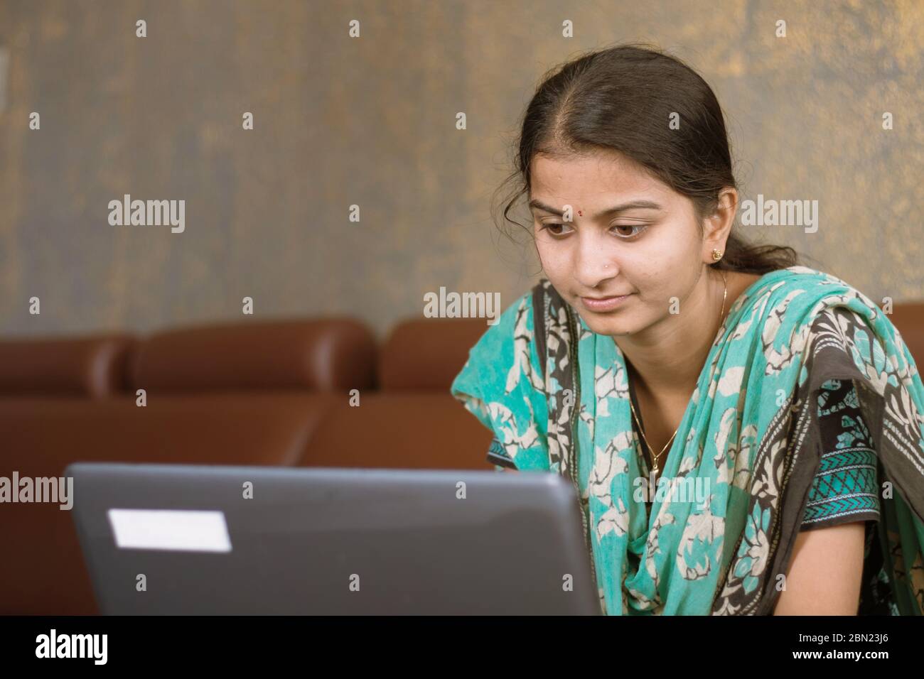 Smiling indian girl student or employee busy on laptop sit at home in casual dress, happy woman studying, e-learning, using online software or Stock Photo