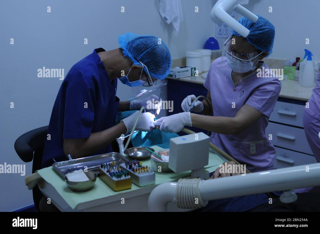 A Cambodian dentist & female dental assistant, both wearing a protective face mask & shield, work on a patient at a dental clinic during the coronavirus pandemic. Phnom Penh, Cambodia. © Kraig Lieb Stock Photo