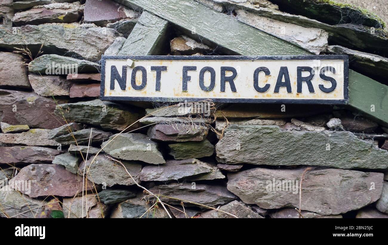 Old metal sign 'Not for Cars' in black letters on a white background indicating a roadway that cars are not permitted to use fixed to an stone wall Stock Photo