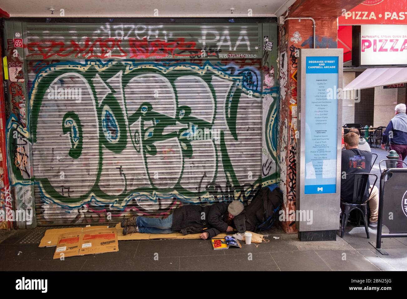 Homeless man sleeping on the ground next to a restaurant in Melbourne, Victoria,Australia Stock Photo