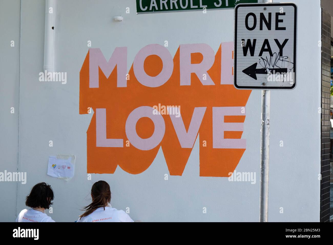 rear viewWomen putting MORE LOVE logo on white wall  in Carroll Street in the Melbourne suburb of Richmond,Victoria, Australia Stock Photo