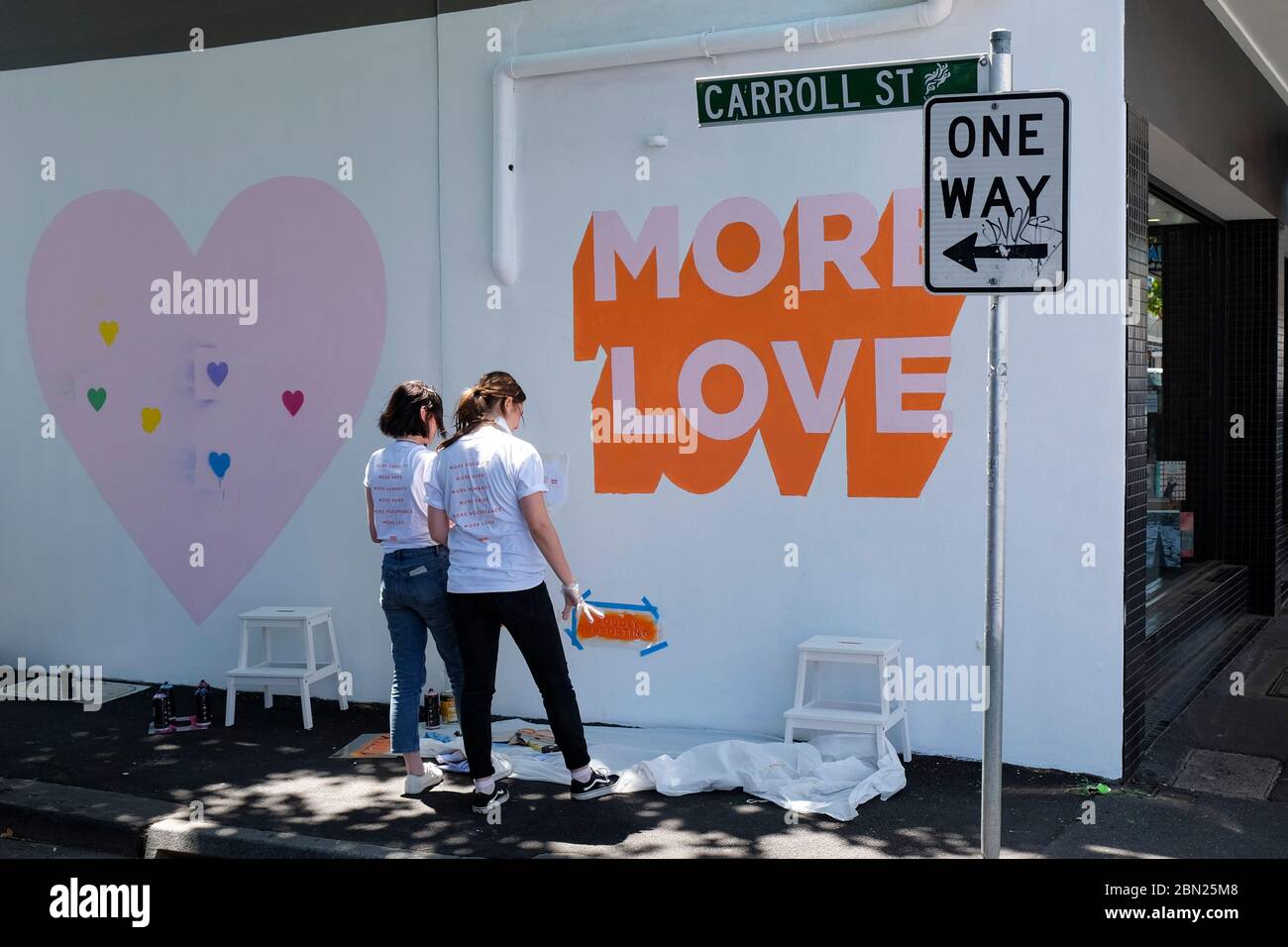 Women putting MORE LOVE logo on white wall  in Carroll Street in the Melbourne suburb of Richmond,Victoria, Australia Stock Photo