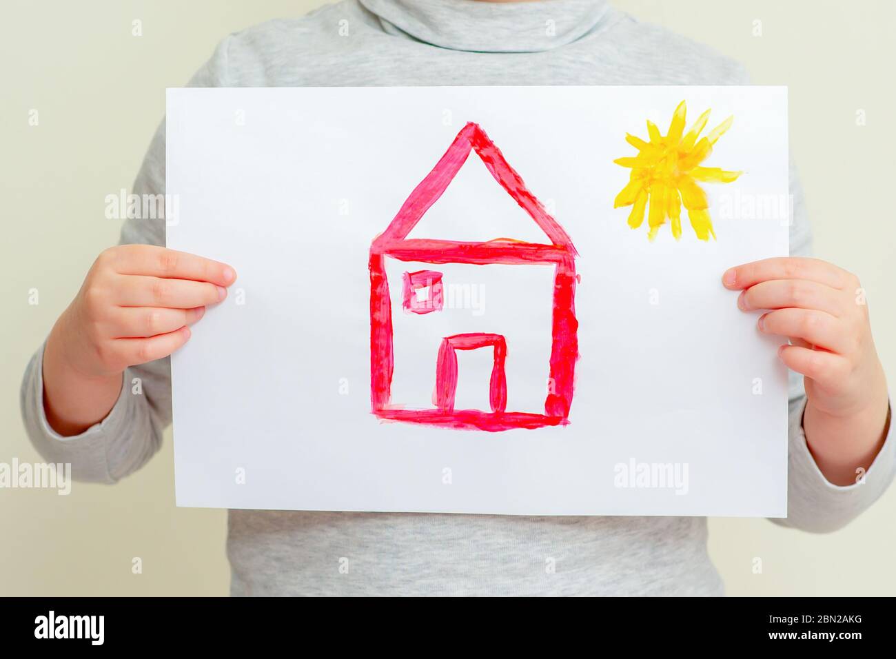 Closeup of child is holding picture of red house with sun at elementary school. Painting concept. Stock Photo