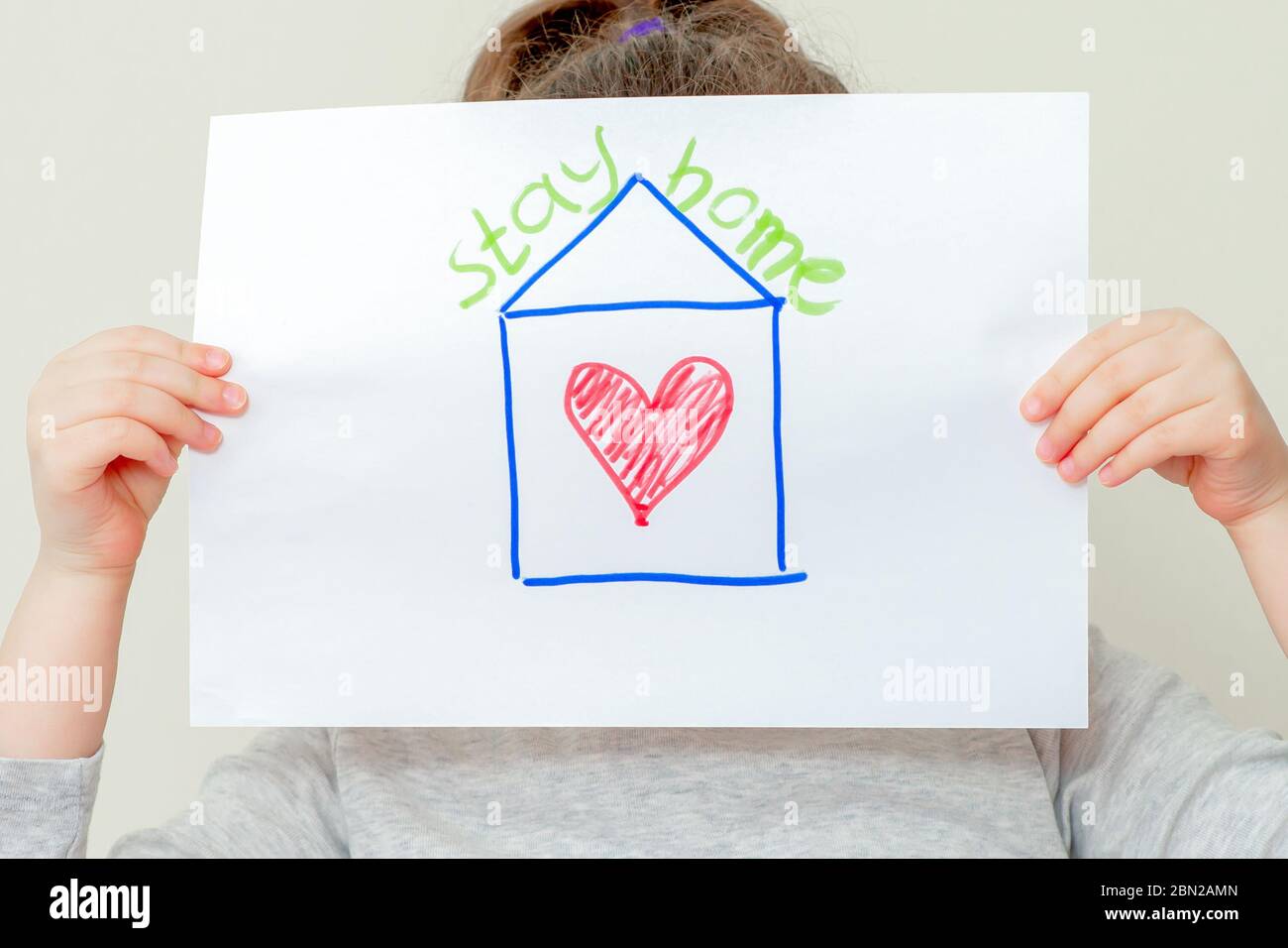 Child's hands holding a picture of house with red heart and words Stay Home. Coronavirus concept. Stock Photo