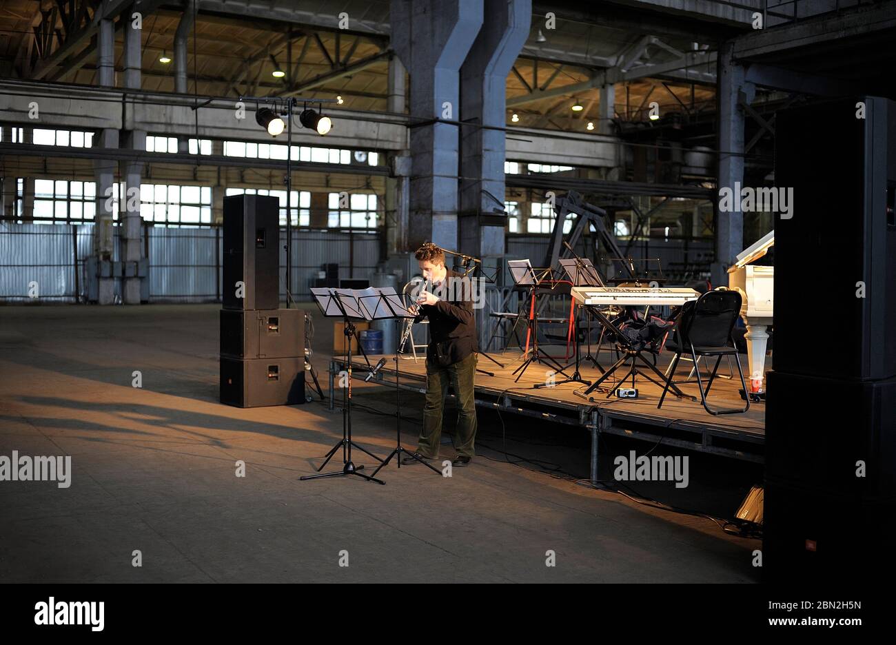 Young man, the musician, playing flute in front of stage in the empty production hall of an old plant Stock Photo