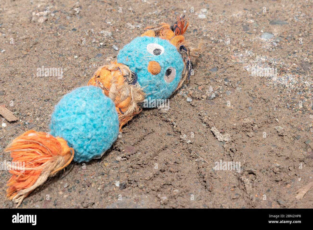 A dirty faded stuffed child's toy lying in dirt. Faint tire tracks from an automobile below the toy. Stock Photo