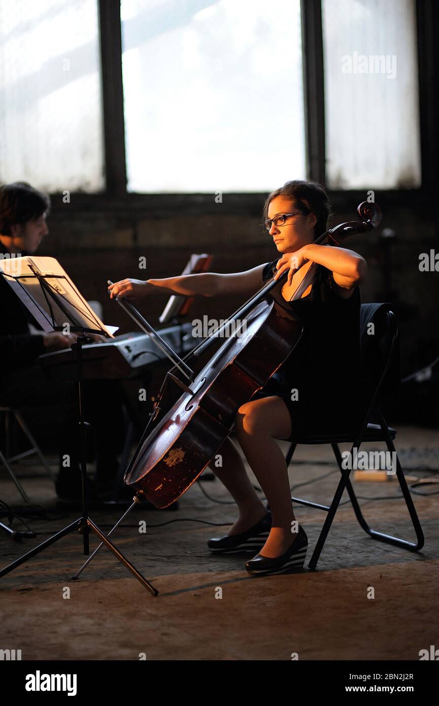 Young female musician playing cello in the production hall of an old plant Stock Photo