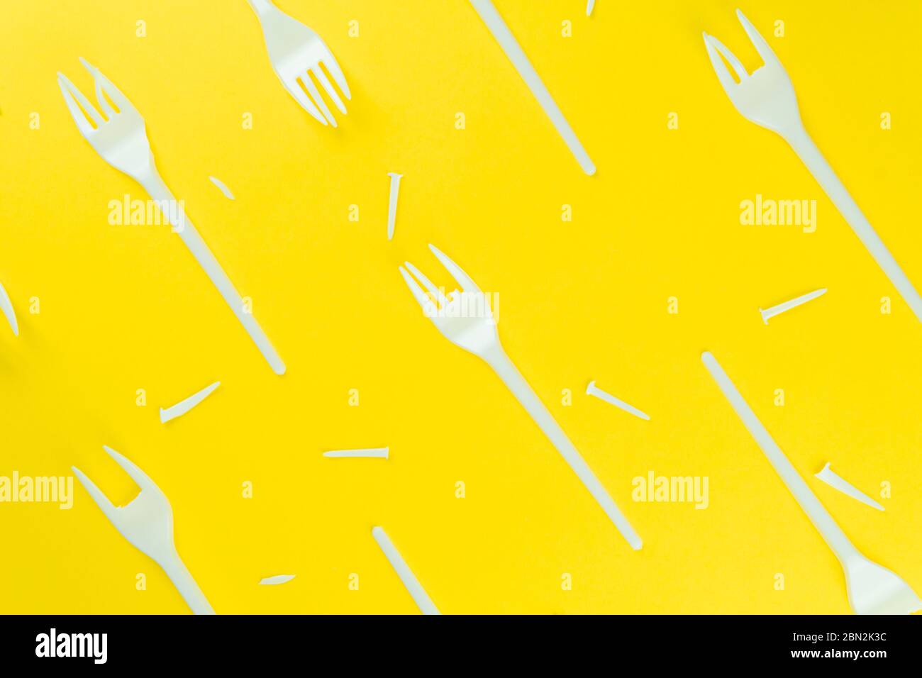 A lot of broken plastic forks on a yellow background. The concept of environmental problems, environmental pollution by plastic waste. Top view. Stock Photo