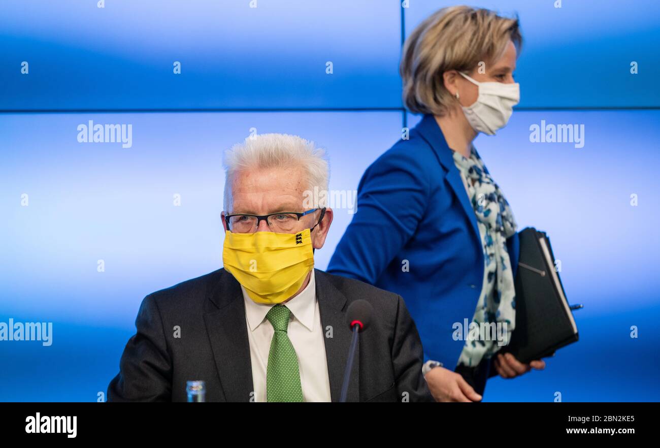 Stuttgart, Germany. 12th May, 2020. Winfried Kretschmann (r, Bündnis 90/Die Grünen), Prime Minister of Baden-Württemberg, is sitting in his seat at a government press conference wearing a protective mask, while behind him, Baden-Württemberg's Minister of Economics Nicole Hoffmeister-Kraut (CDU) passes by. At the press conference, the state government announced new aid for medium-sized businesses. Credit: Christoph Schmidt/dpa/Alamy Live News Stock Photo