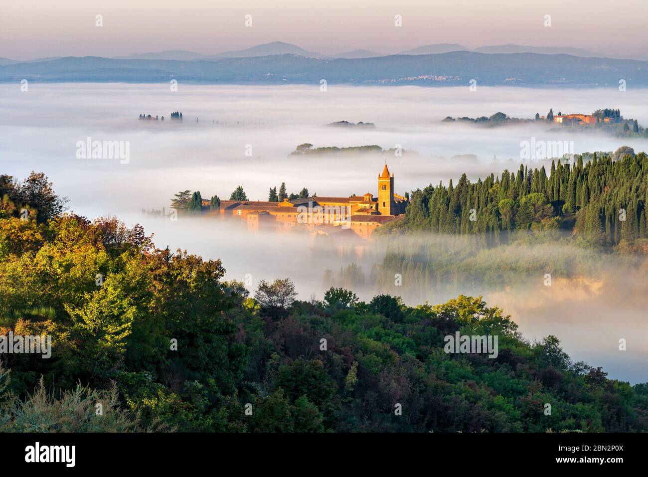 The abbey of Monte Oliveto Maggiore looks like an islands in an ocean of morning fog, crete senesi landscape, Siena, Italy Stock Photo