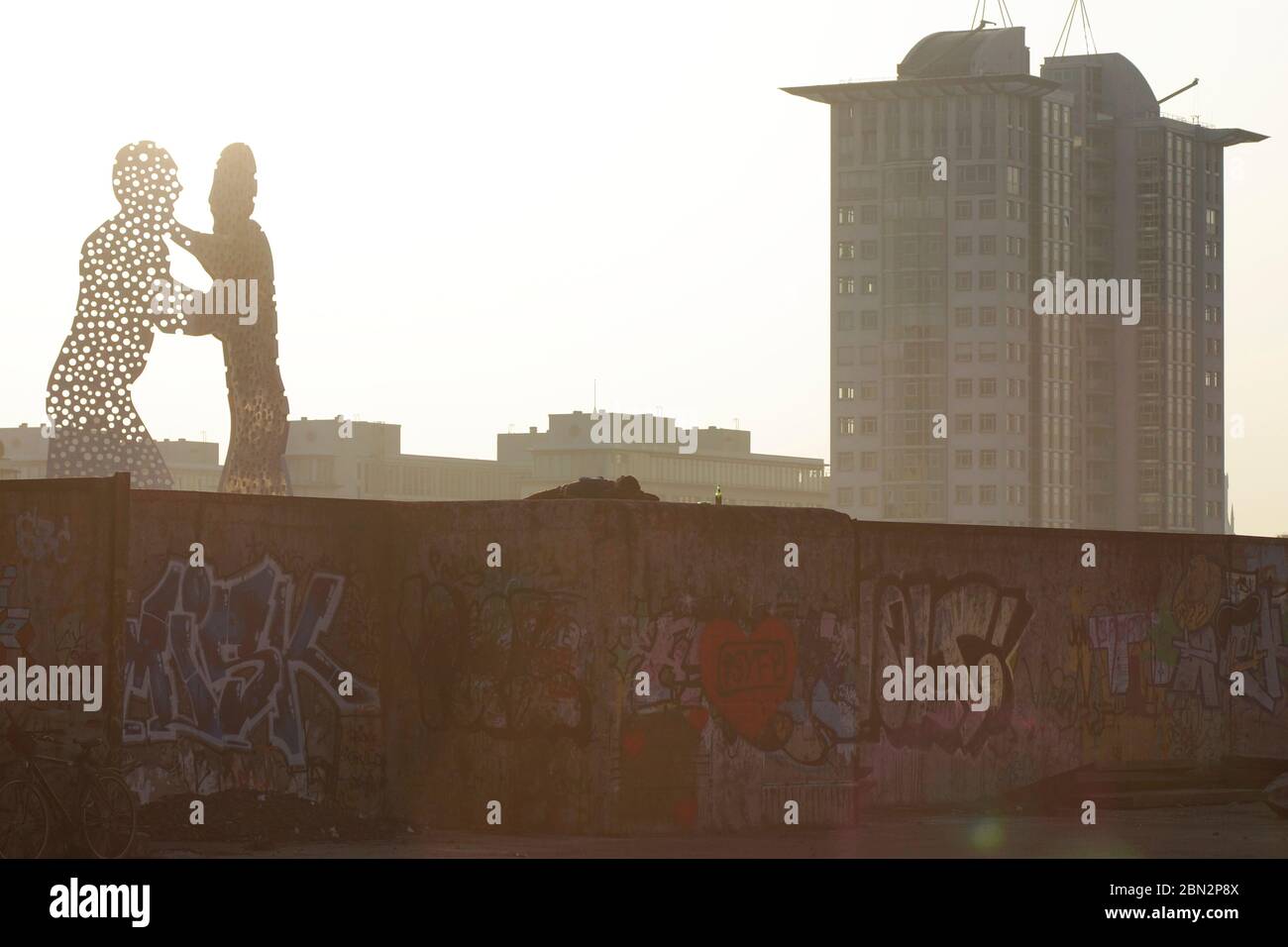Molecule Man an der Spree vor den Treptowers im Vordergrund ein nicht erkennbarer liegender Mann auf  Teilen der alten Grenzanlagen in Berlin. Stock Photo