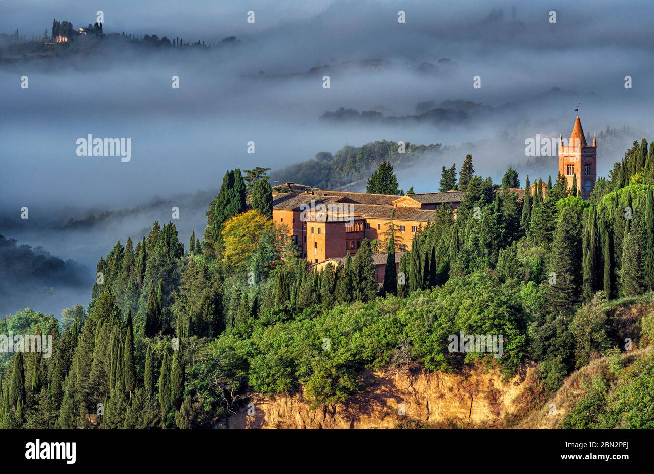 the bell tower of Monte Oliveto Abbey appearings from a dense autumn fog in the crete senesi landscape close to Siena Stock Photo