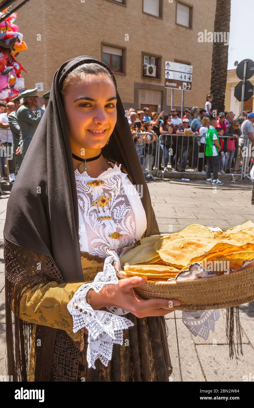 Sardinia festival, a young woman in Sardinian dress carries a basket of traditional bread - pane carasau - during the Cavalcata festival in Sassari Stock Photo