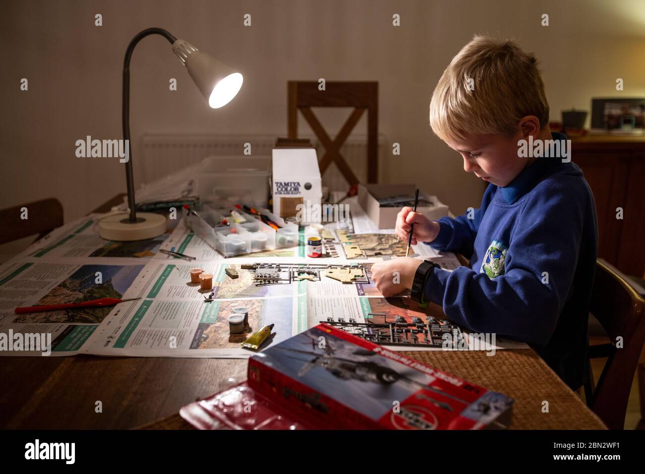 Young boy aged 8 paints parts of an Airfix model kit whilst building a second world war model aircraft at home, London, England,UK Stock Photo