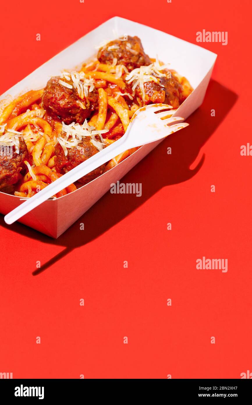 Italian spaghetti and meatballs with tomato sauce in takeaway packaging box on red background with shadow.Restaurant food delivery concept Stock Photo