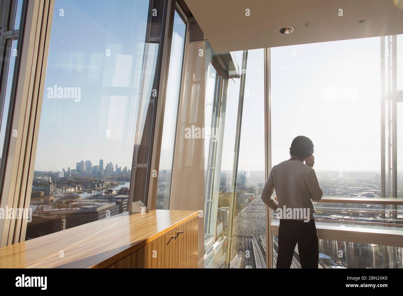 Businessman talking on smart phone at sunny modern highrise window Stock Photo