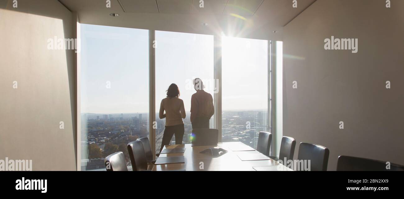 Business people standing at sunny highrise conference room window Stock Photo