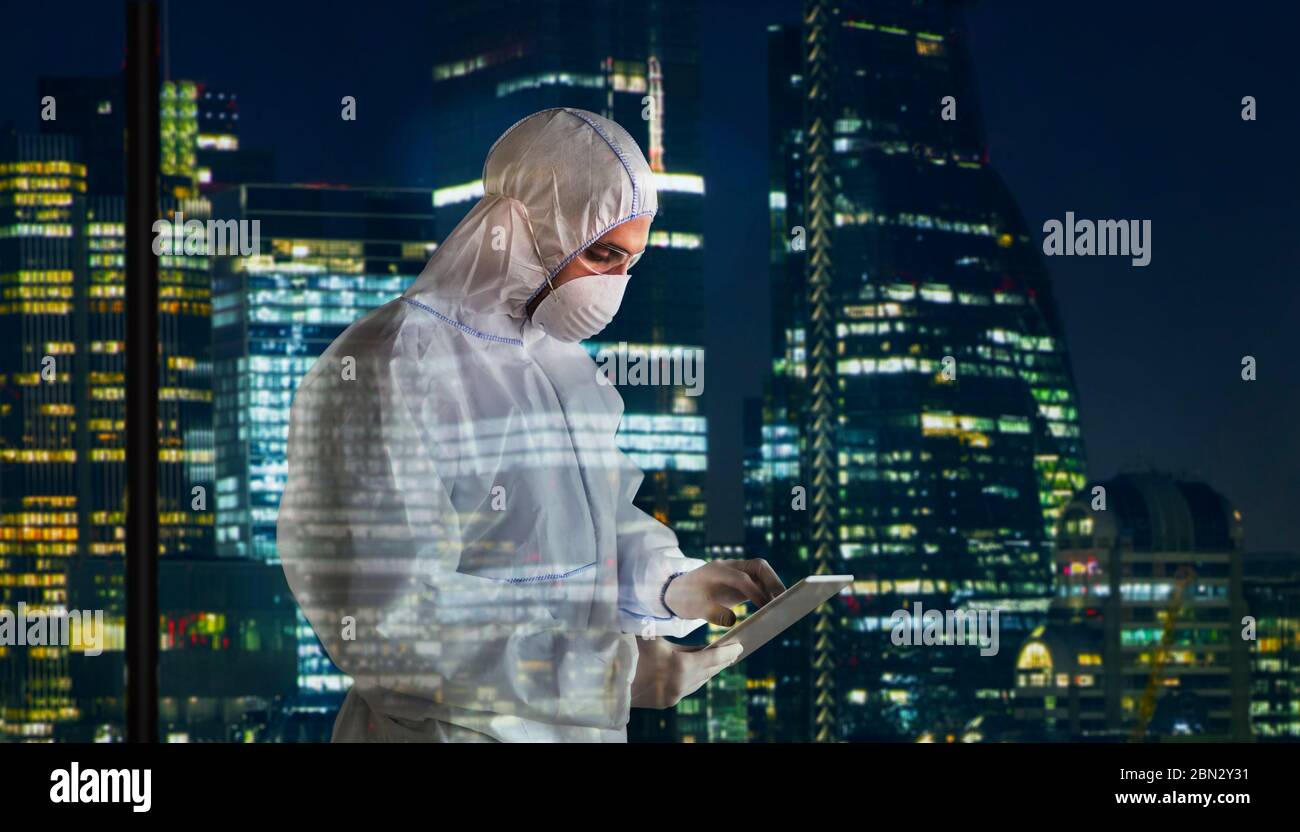 Scientist in clean suit with digital tablet working late city window Stock Photo