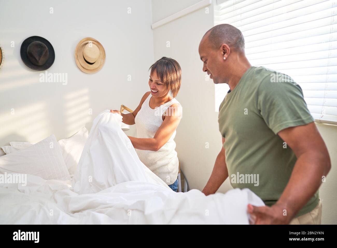 Couple making bed together in bedroom Stock Photo