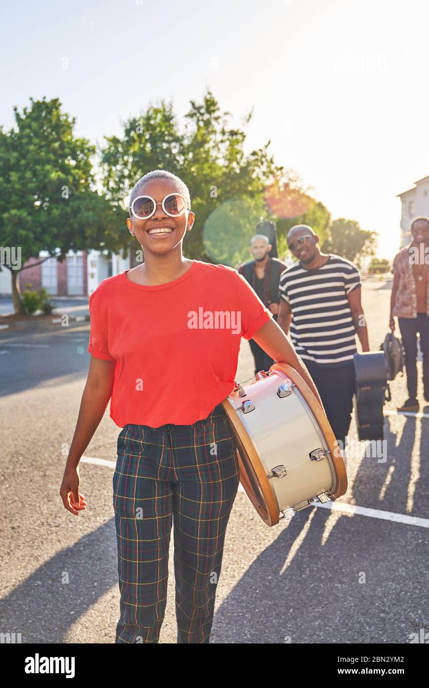Portrait happy female musician carrying drum in sunny street Stock Photo