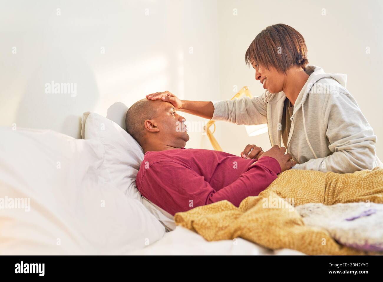 Affectionate wife checking fever of sick husband in bed Stock Photo