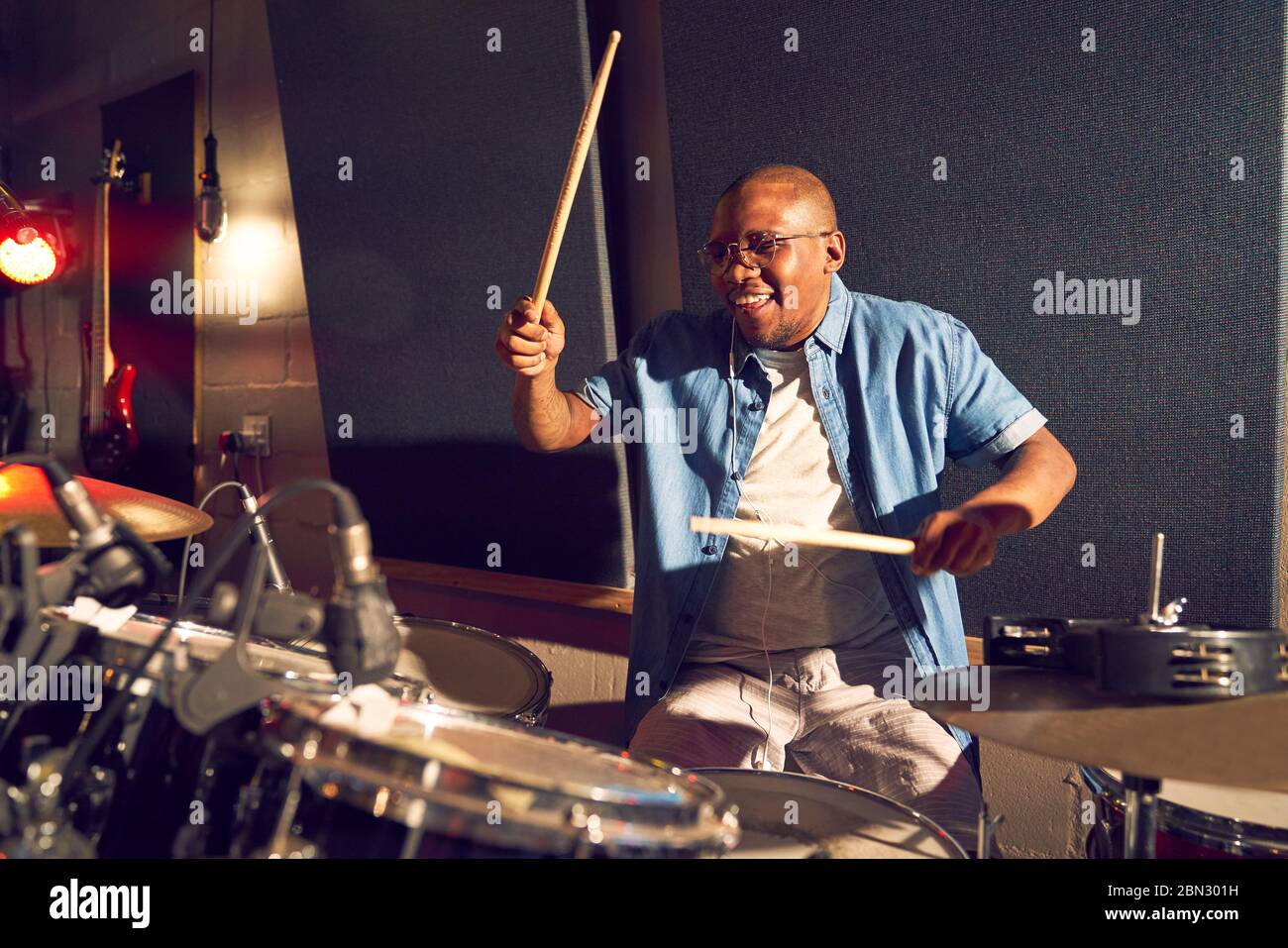Smiling young male drummer playing drums in recording studio Stock Photo